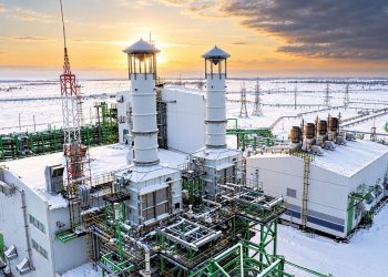 Промышленная установка с двумя белыми башнями на заснеженном нефтегазовом промысле на закате